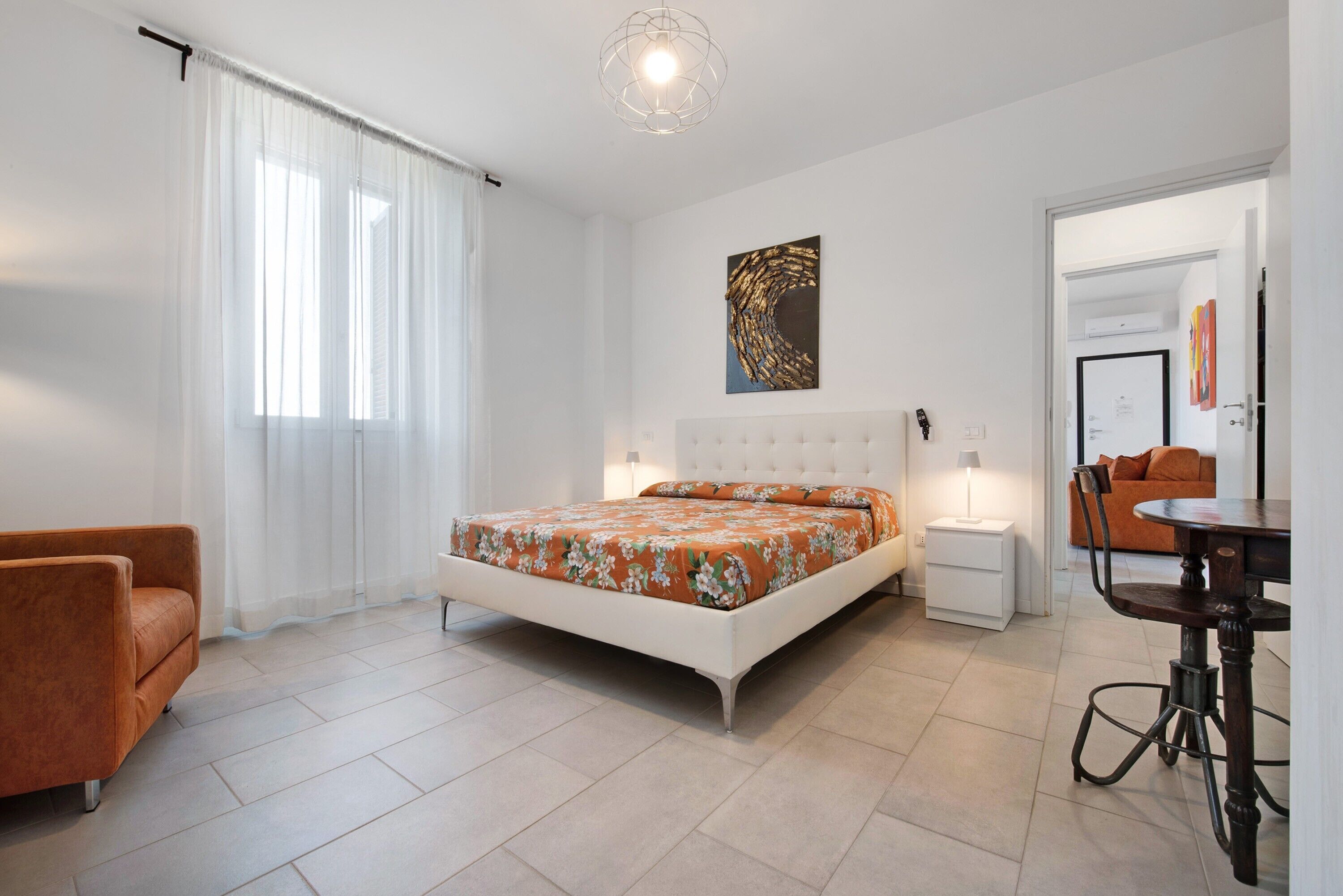 Een moderne slaapkamer met een bed, een stoel, een nachtkastje en een zithoek met een tafel en stoelen.