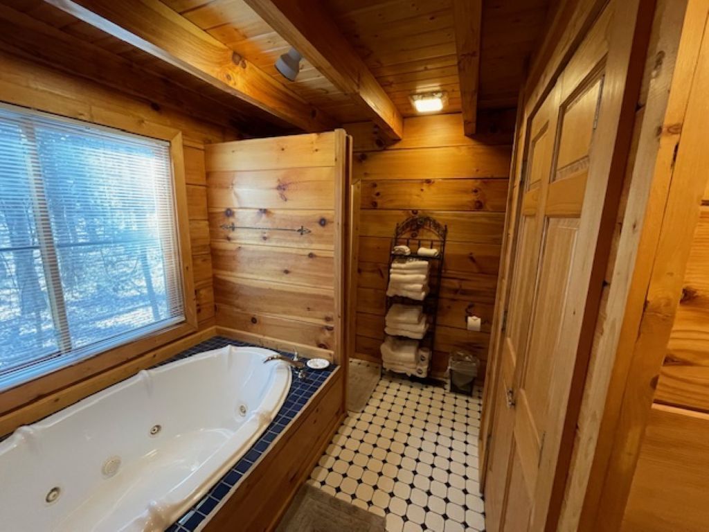 Une salle de bain rustique, avec des murs en bois, une grande baignoire, une fenêtre et un sol carrelé.