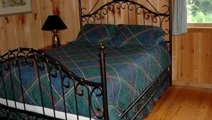 A wooden-paneled room with a metal bed frame, a framed picture on the wall, and a window with curtains.