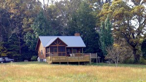 A wooden cabin with a metal roof, a deck, and a fenced yard.