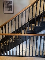 En trappe med sorte spindler og gelænder i træ, der fører til en etage ovenover.