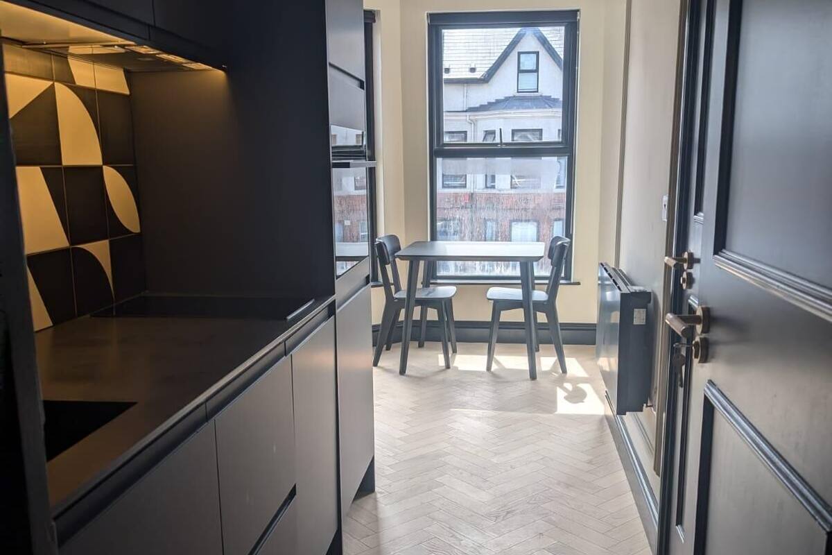 Una cocina moderna con armarios oscuros, piso con diseño en espiga y una zona de comedor con un amplio ventanal que ofrece vistas al exterior.