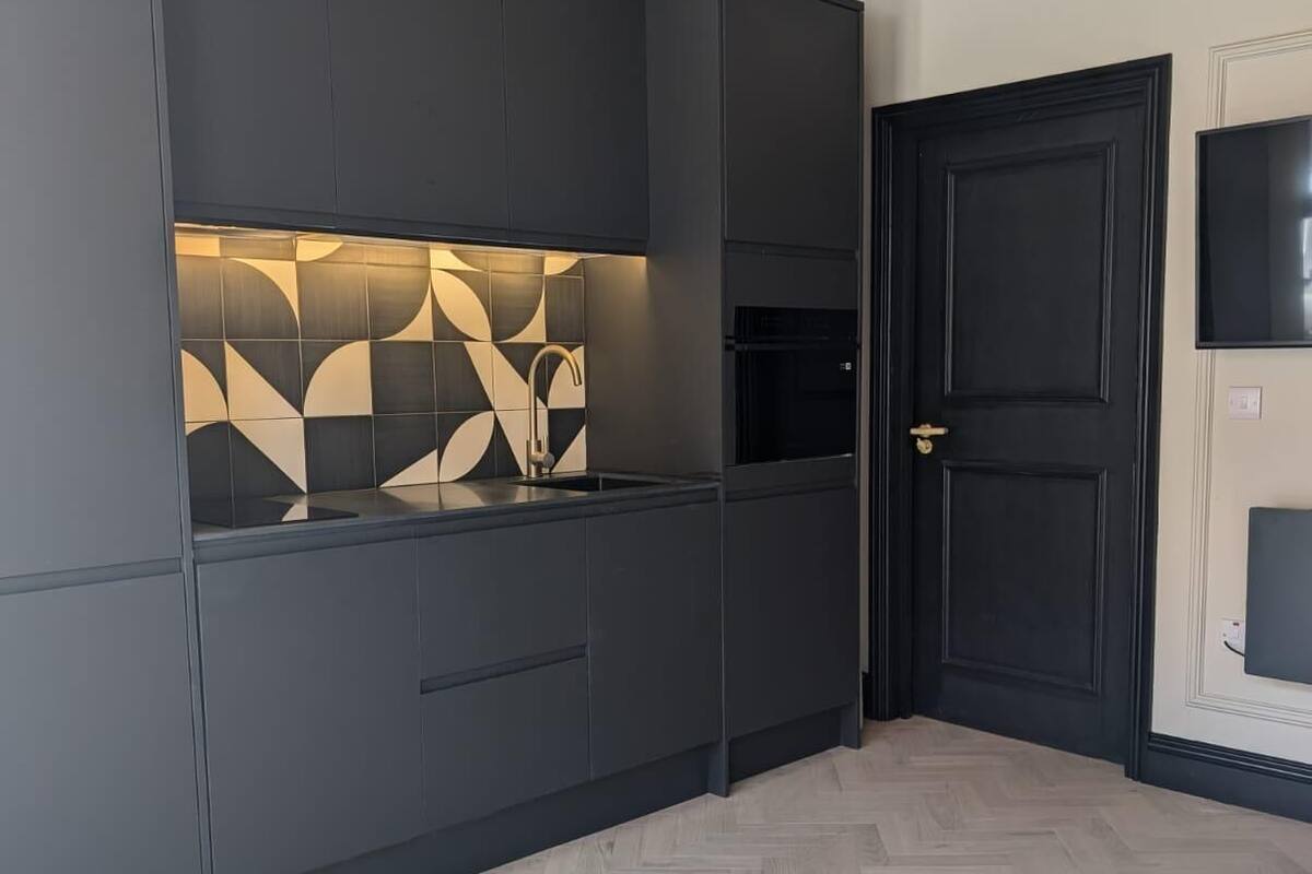 Una cocina moderna con armarios oscuros, un salpicadero con diseño de espiga y una puerta negra.