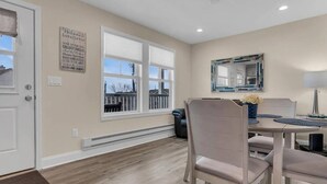 A dining area with a table, chairs, a bench, a mirror, and a window with a view of the outside. - Cozy 1-bedroom condo in Lavallette, located 1 block from beach (Lavallette)