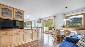 A spacious kitchen with wooden cabinets, a dining area with a table and chairs, and a large window with a view of a forested area. - 1006A Apartments Ciancel Gino (Ortisei)