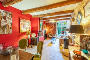 A room with red walls, wooden beams, a dining area with chairs, a table, and a view through a glass door.