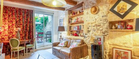 A cozy living room with a sofa, chairs, a table, a bookshelf, and a stone wall.