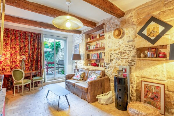 A cozy living room with a sofa, chairs, a table, a bookshelf, and a stone wall.