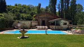 A pool with a fountain, surrounded by a grassy area and a stone wall. There are lounge chairs and a small building with a tiled roof. - House near the canal (Meilhan-sur-Garonne)