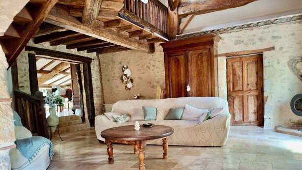 A rustic living room with exposed wooden beams, a patterned sofa, and a round wooden coffee table. - House near the canal (Meilhan-sur-Garonne)