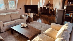 Ein Wohnzimmer mit Sofa, Couchtisch und Fernseher. Es gibt einen Essbereich mit Stühlen und Tisch.