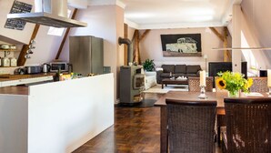 Eine moderne Küche mit einer zentralen Kochinsel, ein Essbereich mit Korbstühlen, eine Couch und ein Kamin.