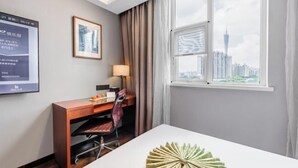 Camera d'albergo con una scrivania, una sedia, una lampada e vista sulla città attraverso un'ampia finestra.