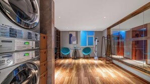 Una camera d'albergo moderna con pavimento in legno, una lavatrice, un piccolo tavolo con sedie e un'ampia finestra.