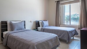 A hotel room with two beds, a window with curtains, and a view of palm trees.