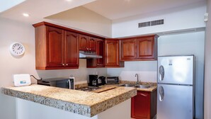 A kitchen with granite countertops, wooden cabinets, a stainless steel refrigerator, a built-in oven, and a clock on the wall.