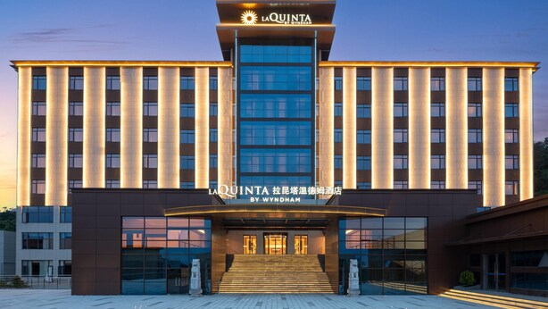 Een hotel met een moderne gevel, met een opvallende ingang met treden die leiden naar een glazen deur, en borden die aangeven dat het La Quinta by Wyndham is.