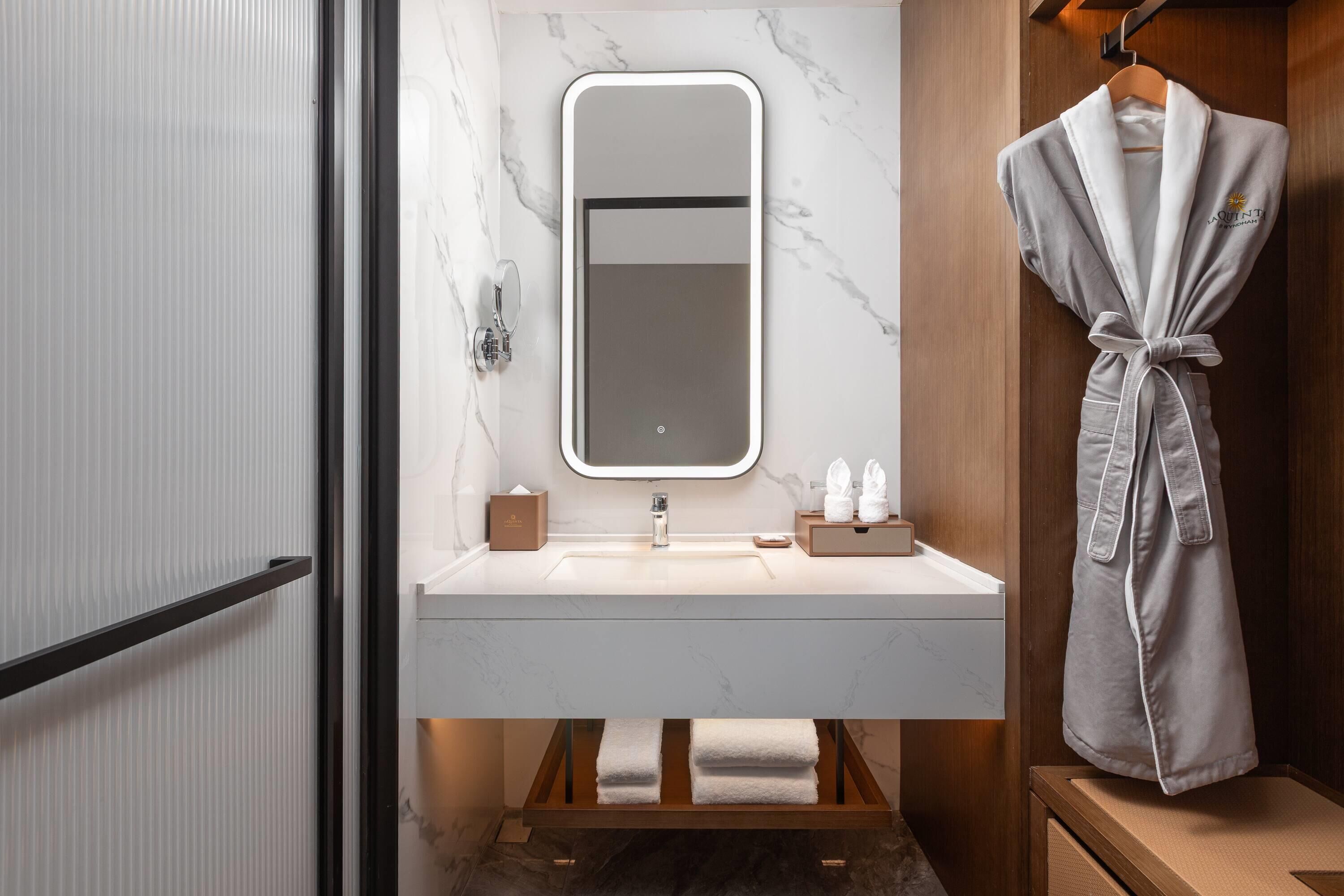 Une salle de bain moderne avec un lavabo en marbre, un grand miroir et un peignoir accroché au mur.