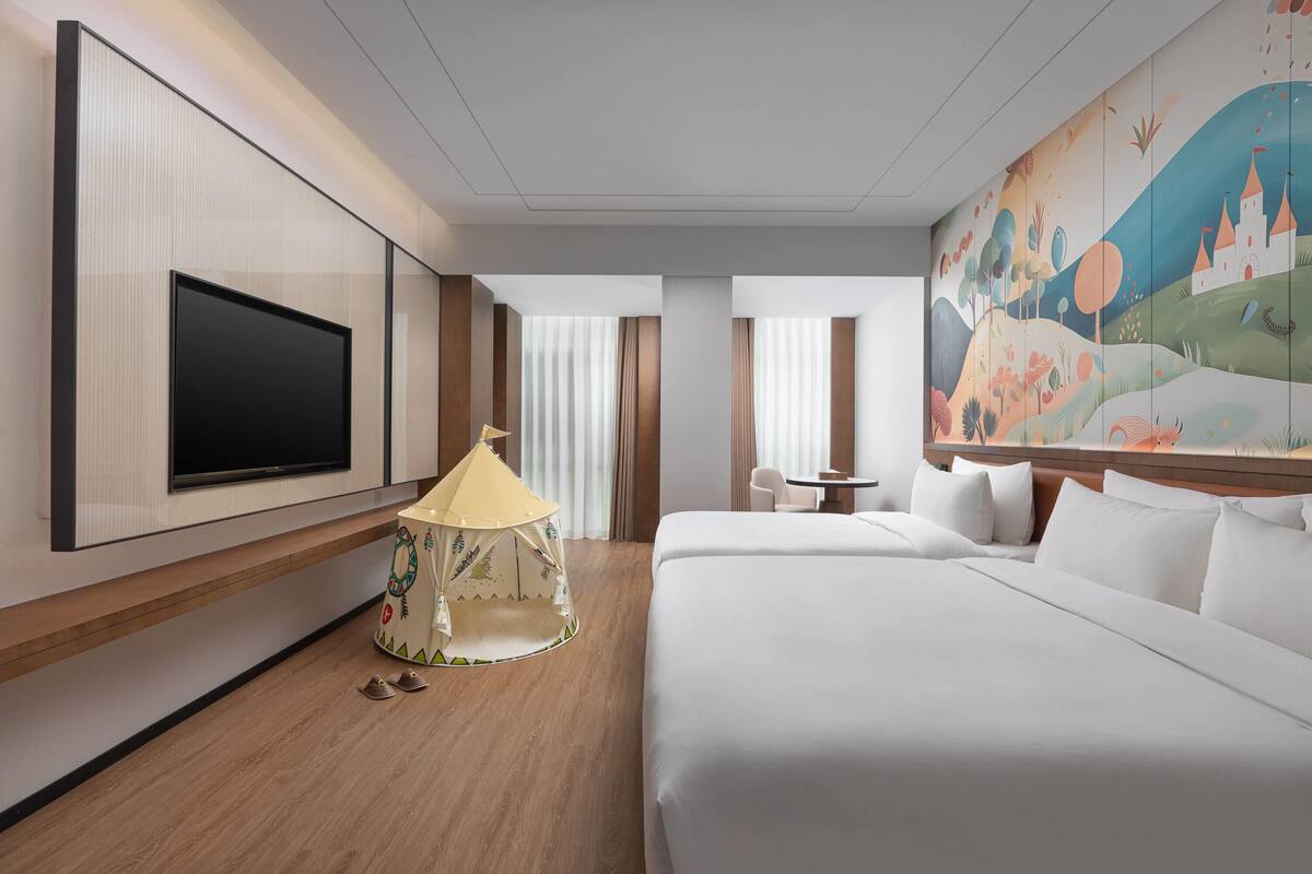 Une chambre d’hôtel équipée d’un grand téléviseur à écran plat, d’un lit, d’une petite table, d’une structure ressemblant à une tente et d’une fresque murale.