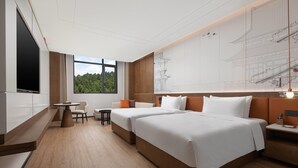 Een hotelkamer met twee bedden, een zithoek met een tafel en stoelen, een groot raam met uitzicht op groen, en een tv aan de muur.