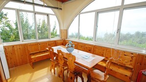 A wooden dining area with a table and chairs, large windows, and a view of greenery outside. - La Corte No.3 (Massa Lubrense)