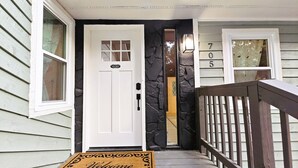 Una entrada de casa con una puerta blanca, felpudo y pared de piedra.