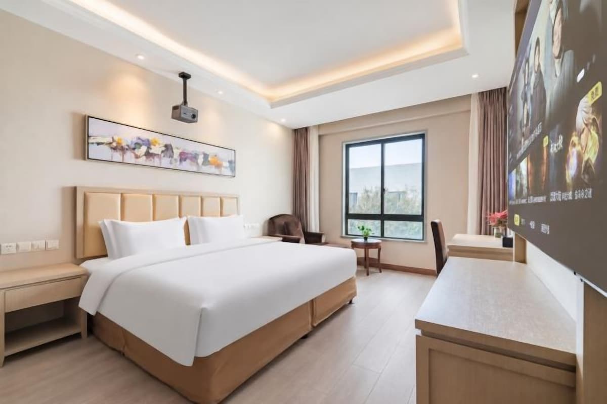 Une chambre d’hôtel avec un grand lit, un bureau, une chaise, une télévision et une fenêtre donnant sur la ville.