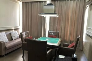 Habitación de hotel con sofá, una mesa con un juego de mesa, lámpara y cortinas.
