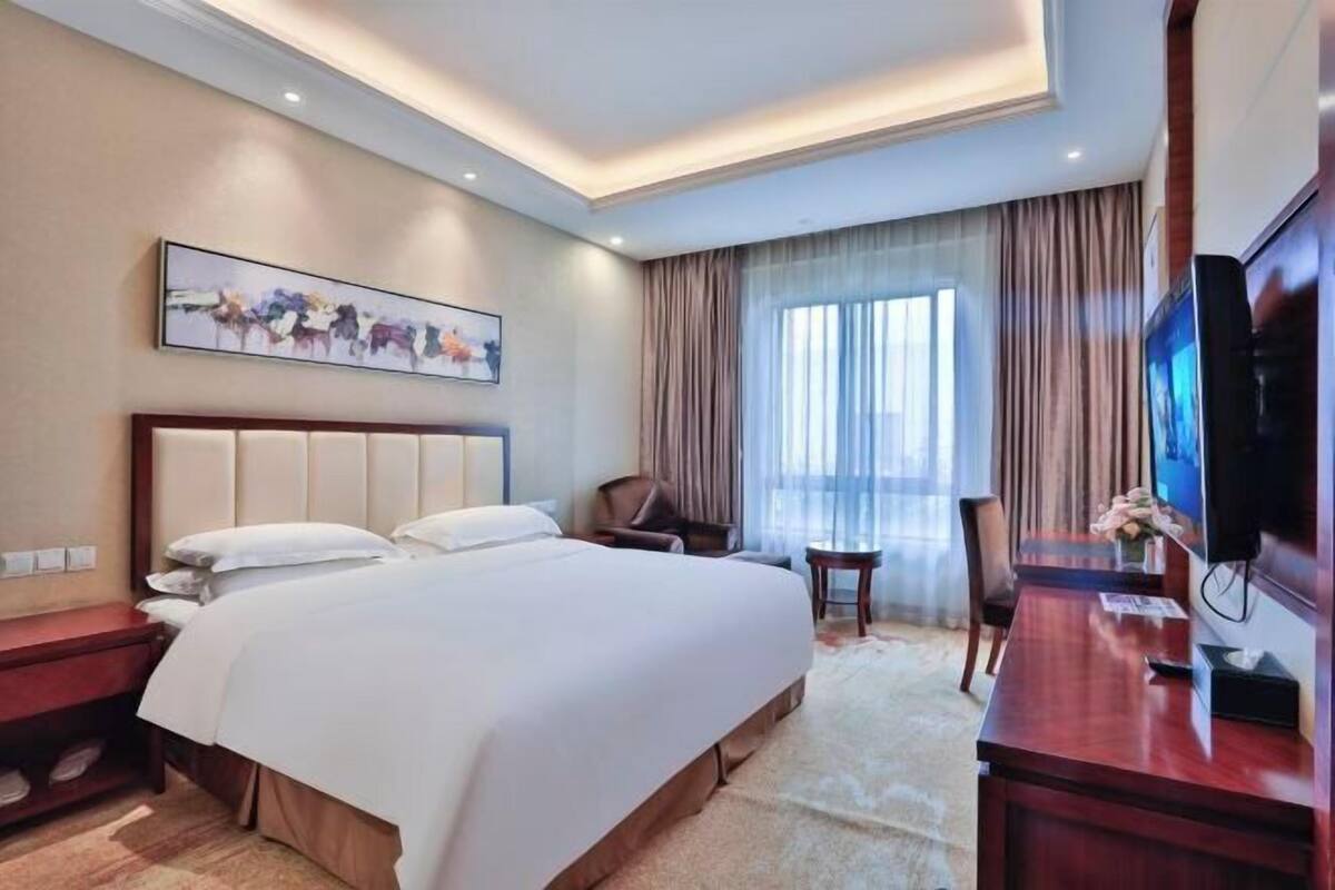 Een hotelkamer met een bed, een bureau, een stoel, een televisie en een schilderij aan de muur.
