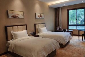 Habitación de hotel con dos camas, un escritorio, una silla y un ventanal grande.