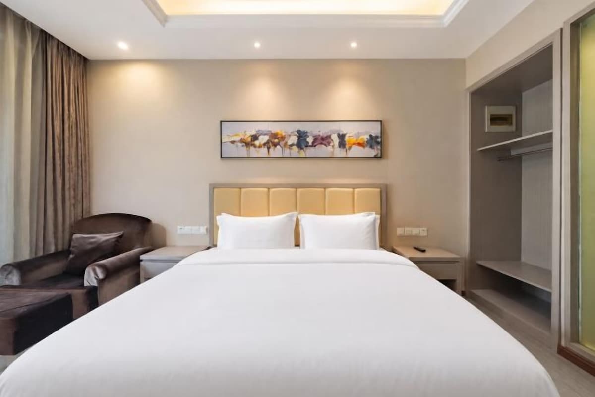 Une chambre d’hôtel avec un grand lit, une table de chevet, une chaise, une armoire et un tableau au mur.