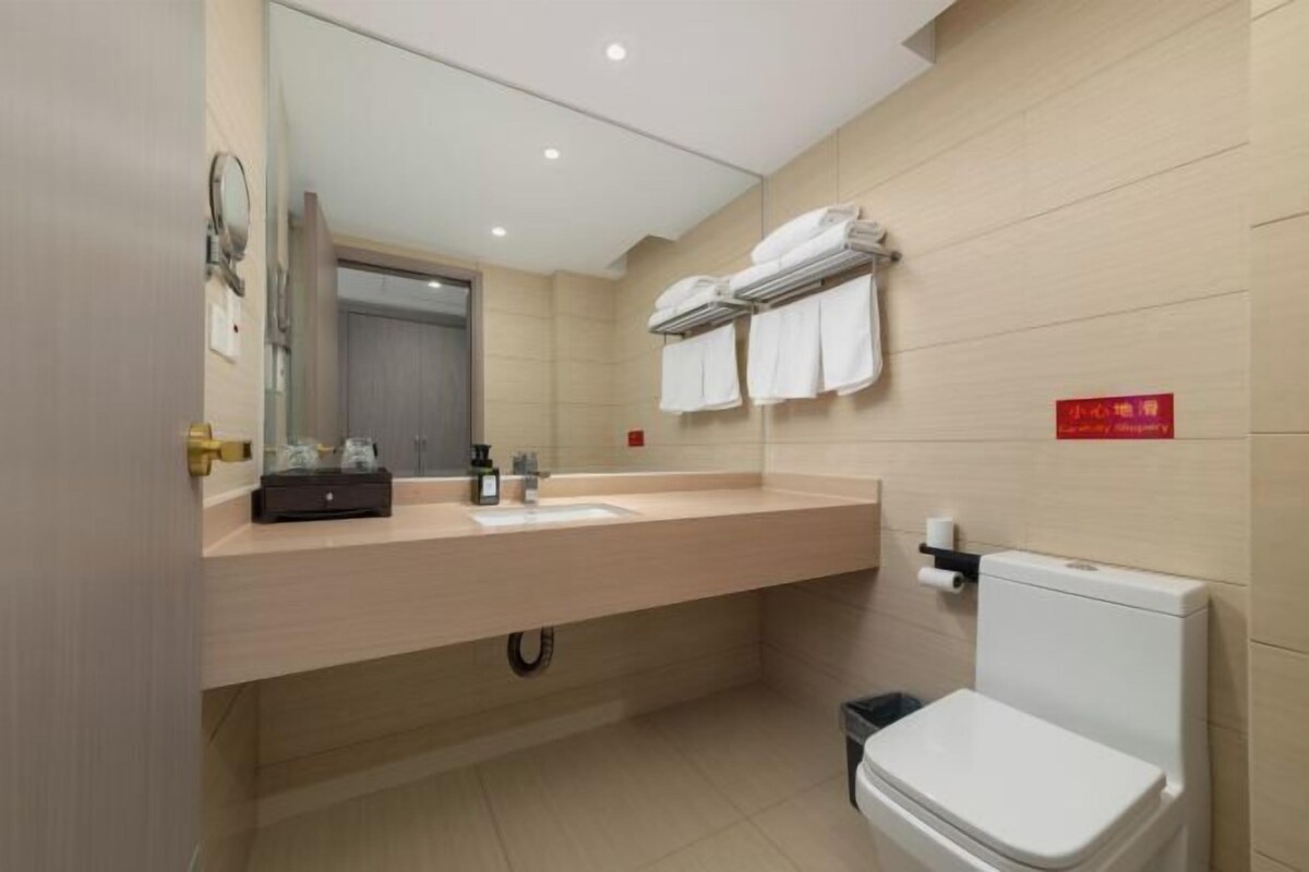 Ein modernes Badezimmer mit einer beige gefliesten Wand, einem weißen Waschbecken, einem Spiegel und einer Toilette. Handtücher hängen über der Toilette an einem Wäscheständer.