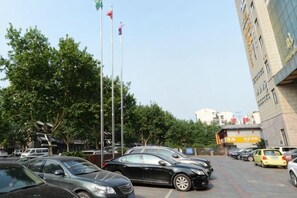 A parking lot with multiple cars, a flagpole with flags, and a building with signage.