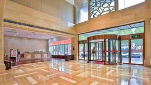 Un hall d’entrée spacieux avec un plancher en bois poli, un comptoir de réception et une entrée en verre surmontée d’un tapis rouge.