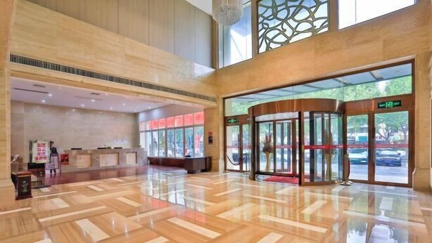 Un hall d’entrée spacieux avec un plancher en bois poli, un comptoir de réception et une entrée en verre surmontée d’un tapis rouge.