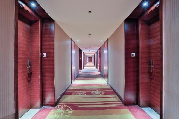 A hotel corridor with wooden doors, a carpeted floor, and a ceiling light fixture.