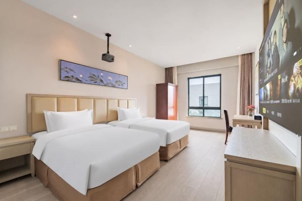 Une chambre d’hôtel avec deux lits, un bureau, une grande fenêtre et un téléviseur fixé au mur.