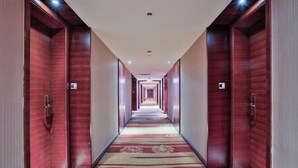 Un couloir d’hôtel avec des portes en bois, une moquette à motifs et des luminaires encastrés.