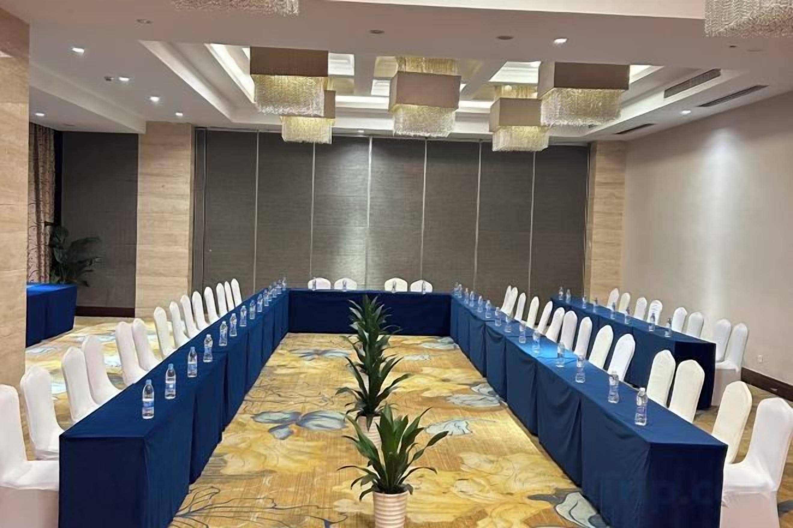 A conference room with a long table, white chairs, and a blue tablecloth.