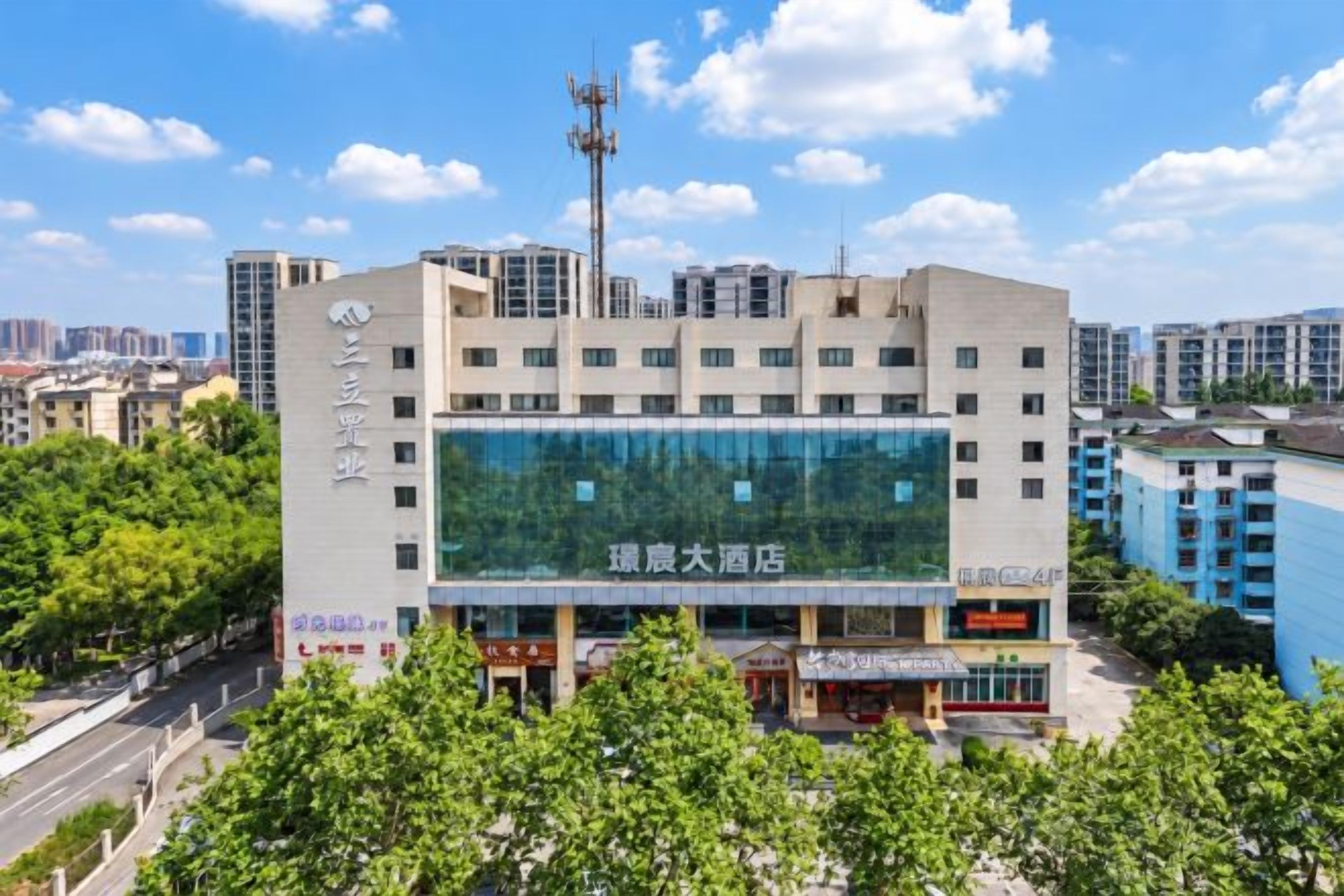 A multi-story hotel with a large glass facade, surrounded by greenery and other buildings.
