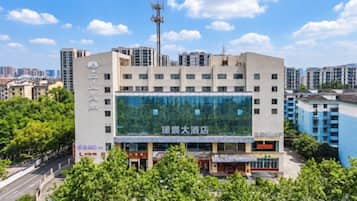 A multi-story hotel with a large glass facade, surrounded by greenery and other buildings.
