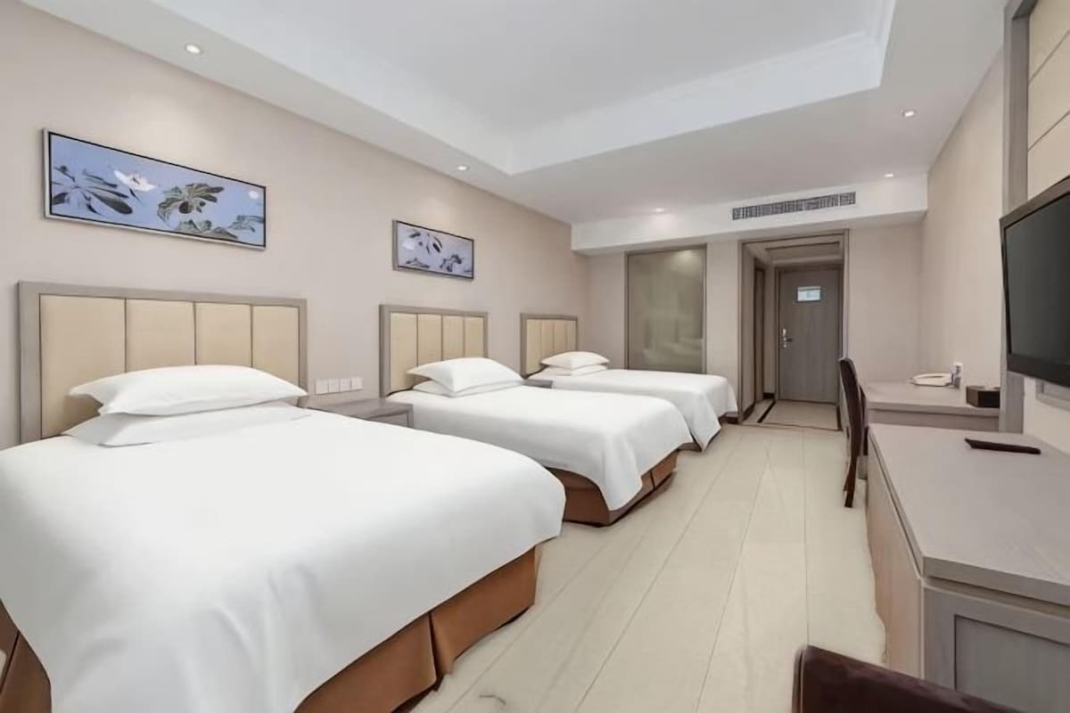 Une chambre d’hôtel avec trois lits, une télévision et des œuvres d’art accrochées aux murs.