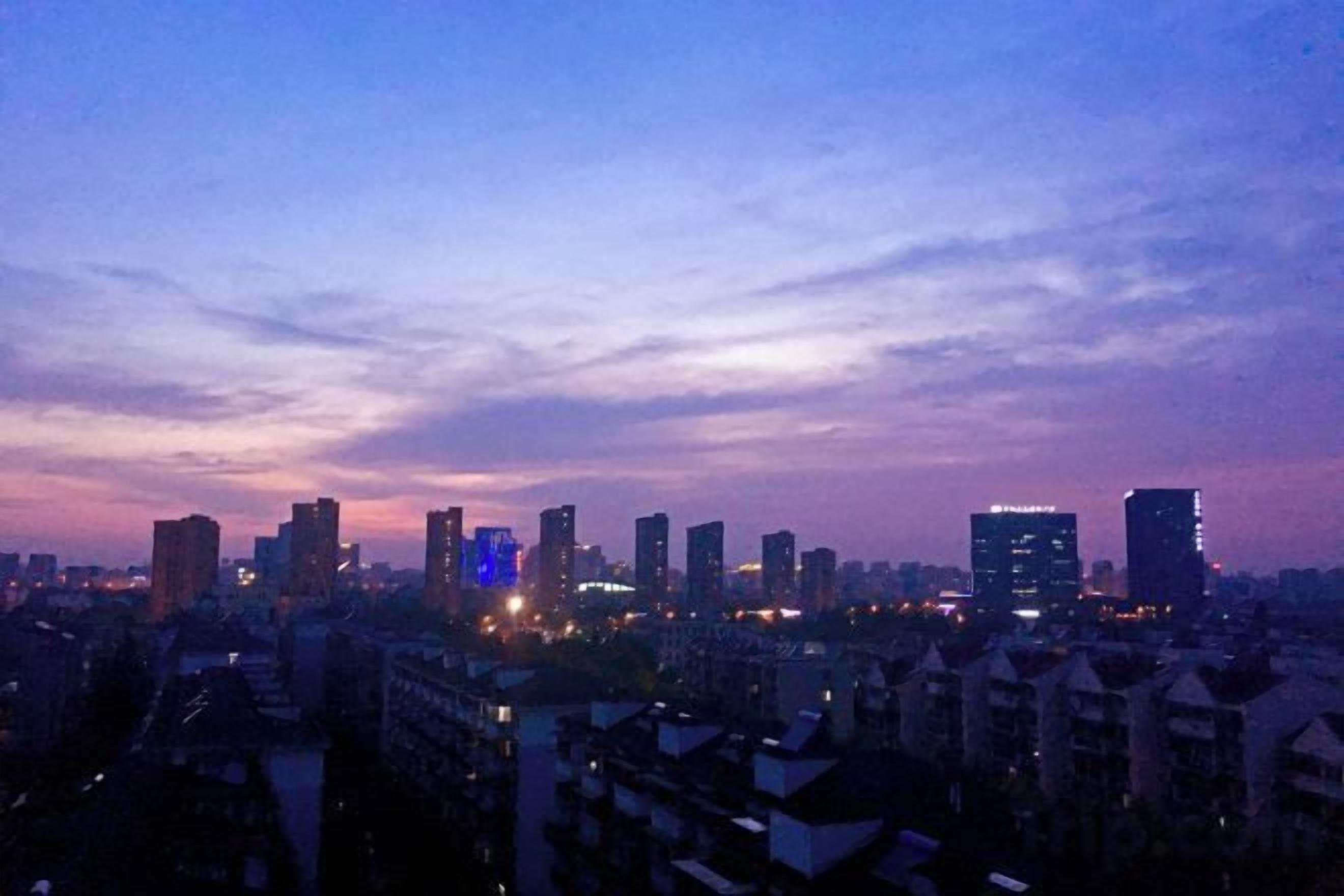 A cityscape at dusk with illuminated buildings and a clear sky.