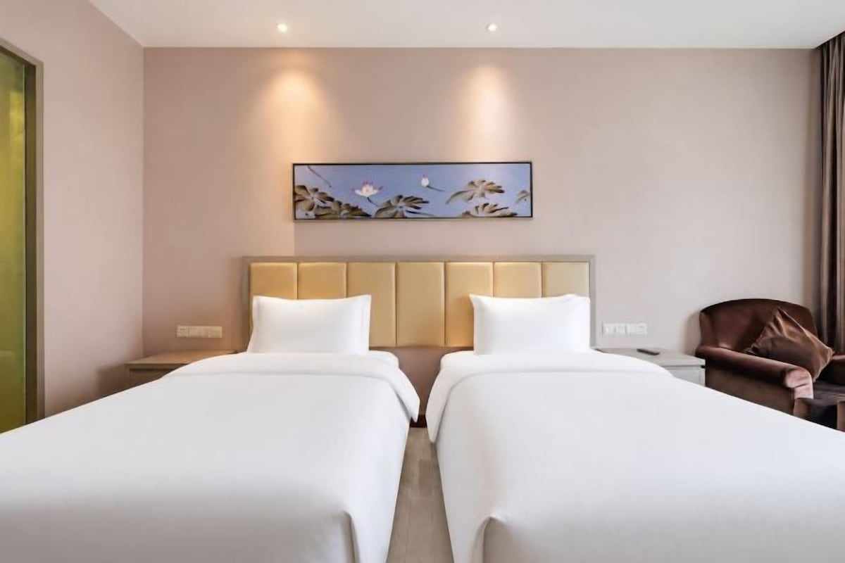 Une chambre d’hôtel avec deux lits, une tête de lit, une table de chevet, une chaise et un tableau au mur.