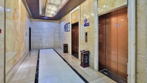 Un couloir au sol en marbre, doté de deux ascenseurs, chacun ayant une porte et une petite plaque.