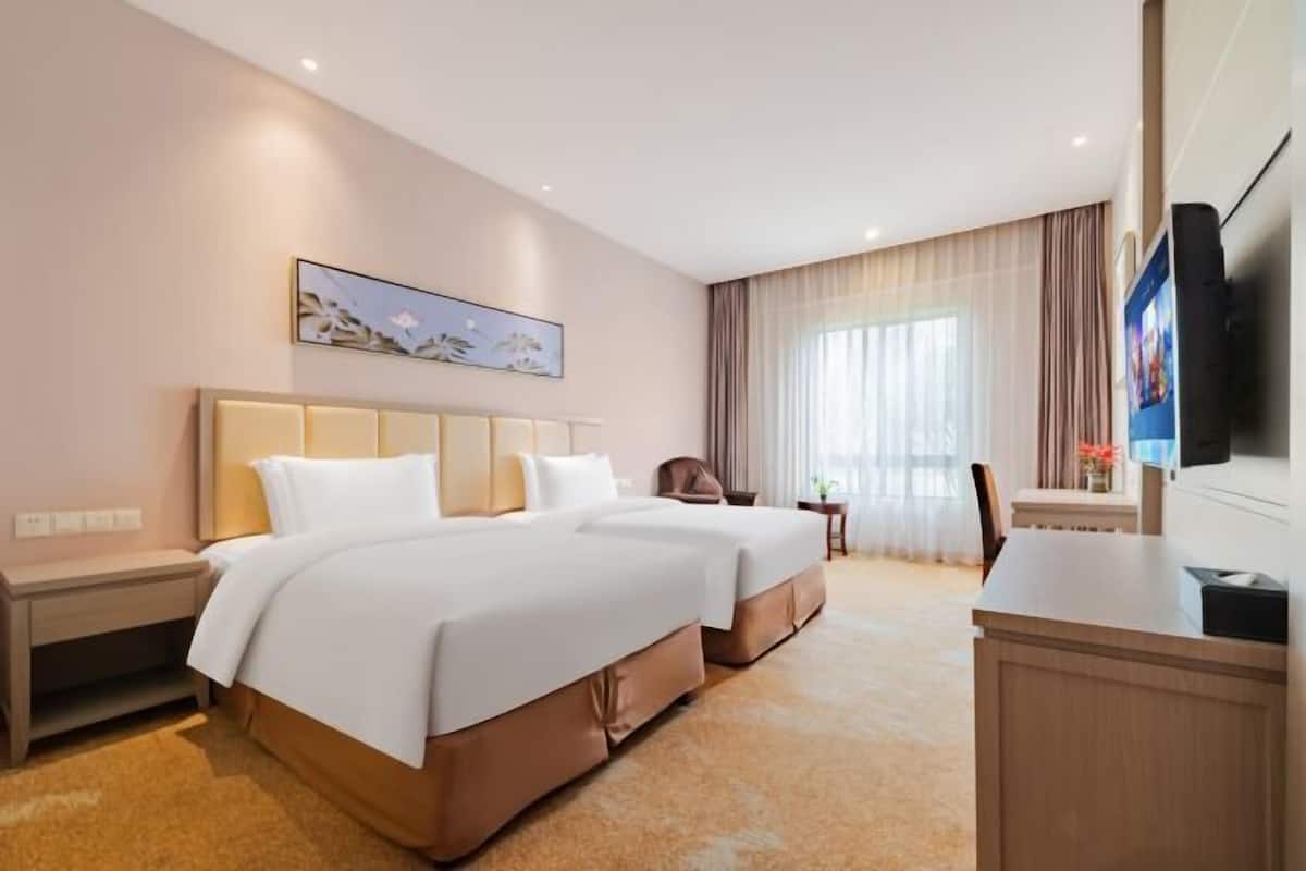 Een hotelkamer met twee bedden, een televisie, een bureau en een schilderij aan de muur.