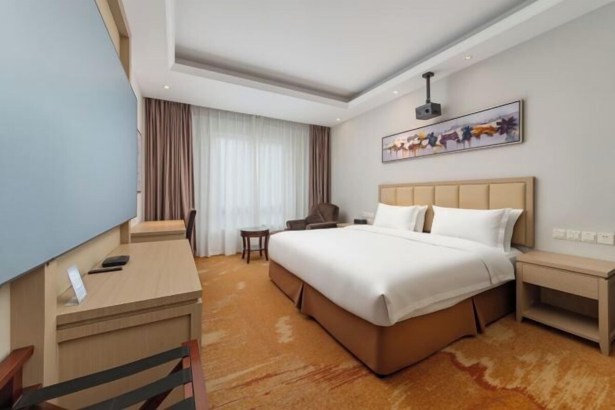 Ein Hotelzimmer mit einem großen Bett, einem Schreibtisch, einem Stuhl, einem kleinen Tisch und einem Fernseher.