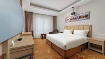 A hotel room with a large bed, a desk, a chair, a small table, and a TV.