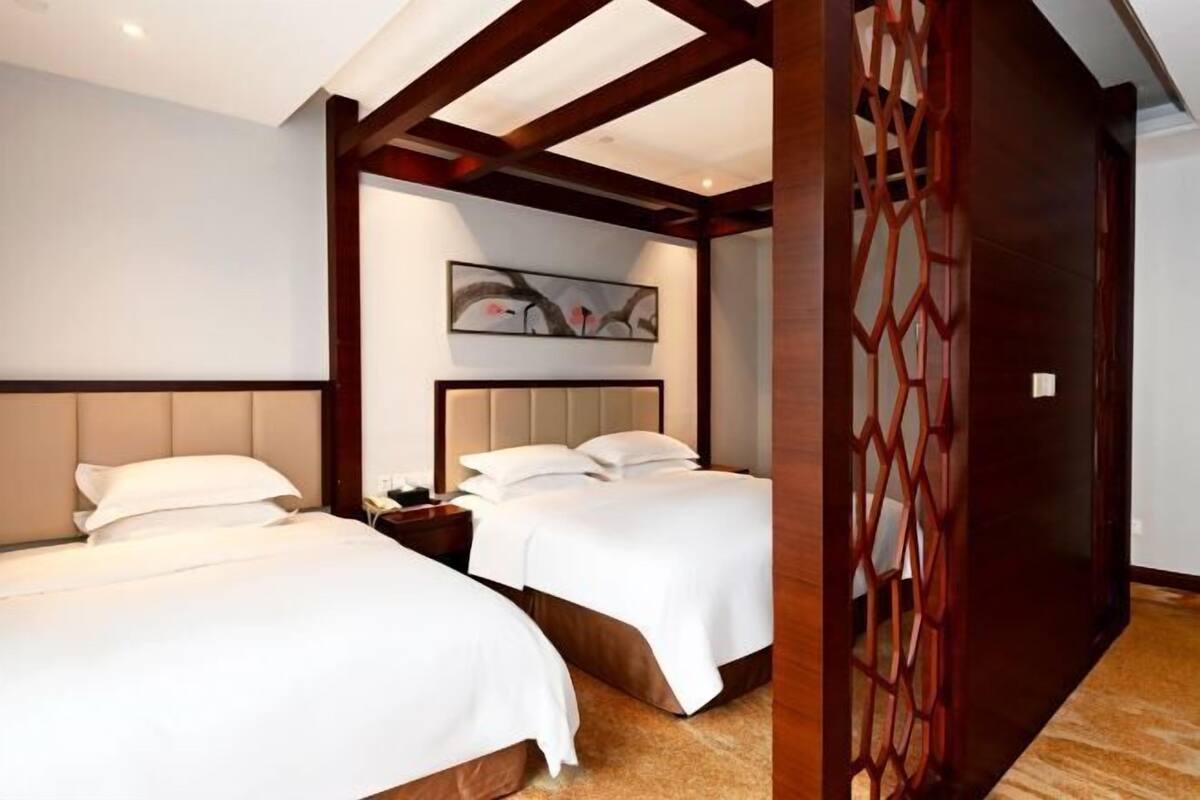 Een hotelkamer met twee bedden, een hoofdeinde, een nachtkastje, een decoratief paneel en een houten scheidingswand.