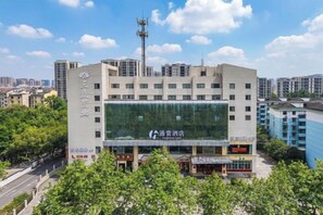 Un hotel de varios pisos con un amplio frente de vidrio, rodeado de vegetación y otros edificios.